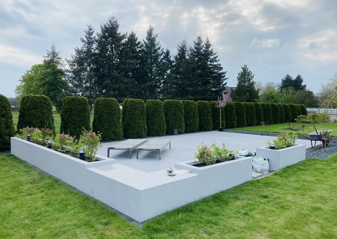 Moderne Gartengestaltung mit Terrasse, Liegestühlen und einer Hecke.