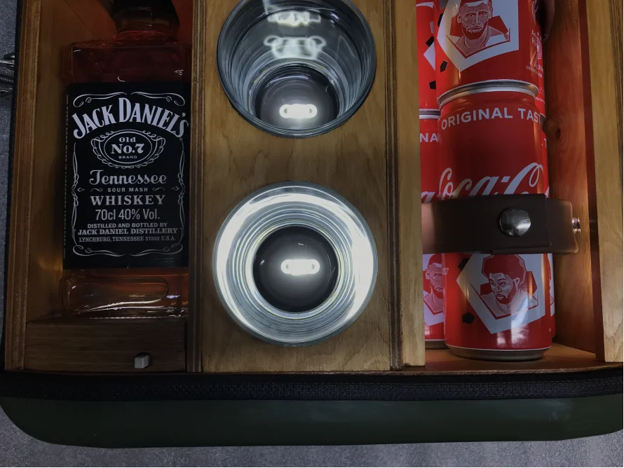 Eine Holzkiste mit einer Flasche, zwei Gläsern und Dosen.