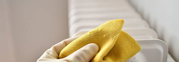 Hand mit gelbem Tuch reinigt Heizung
