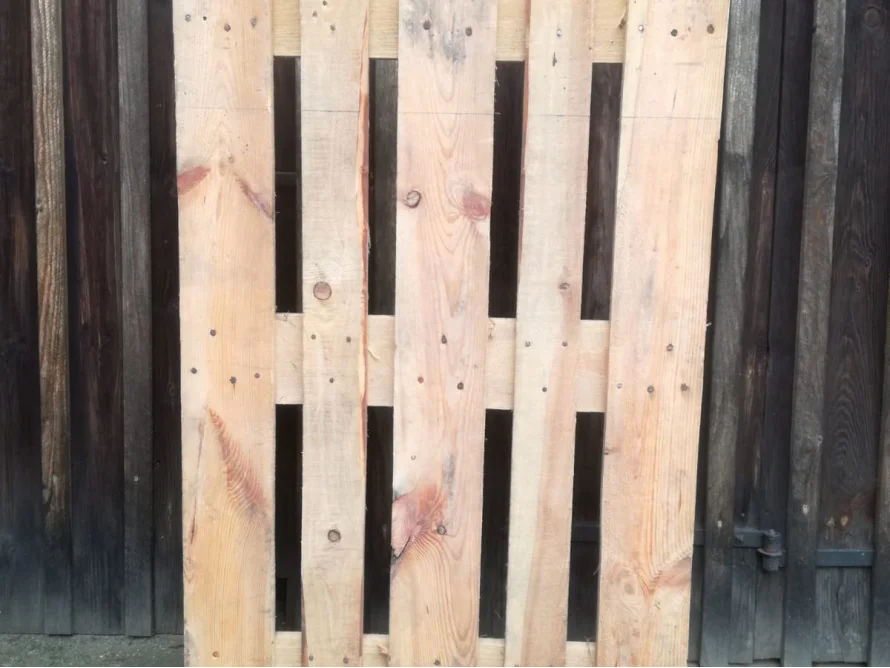 Eine Holzpalette lehnt an einer Holzwand.