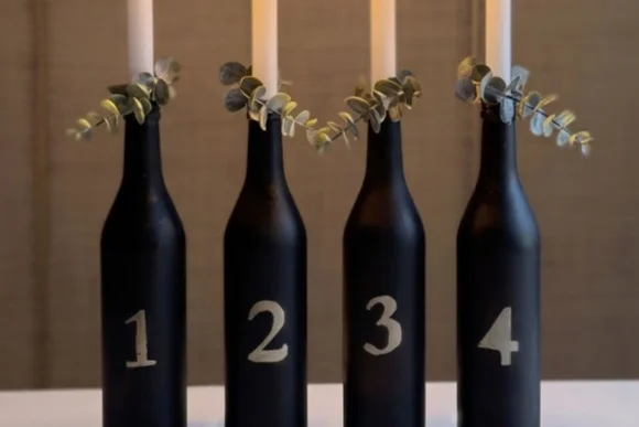 Vier schwarz bemalte, nummerierte Flaschen mit Kerzen als moderner Adventskranz.