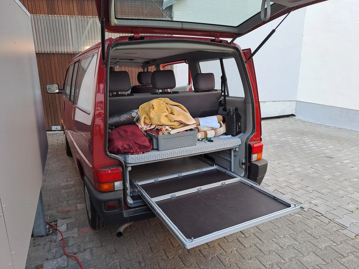 Geöffneter Kofferraum eines roten Vans mit ausziehbarem Ladeboden.