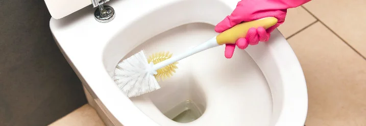 Person mit Handschuh reinigt Toilette mit Klobürste