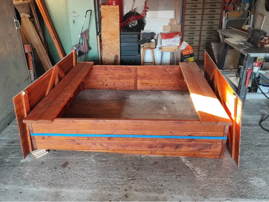 Ein neu gebauter Sandkasten aus Holz mit Sitzbänken.