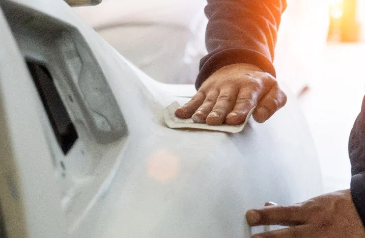 Person schleift Auto mit Schleifpapier