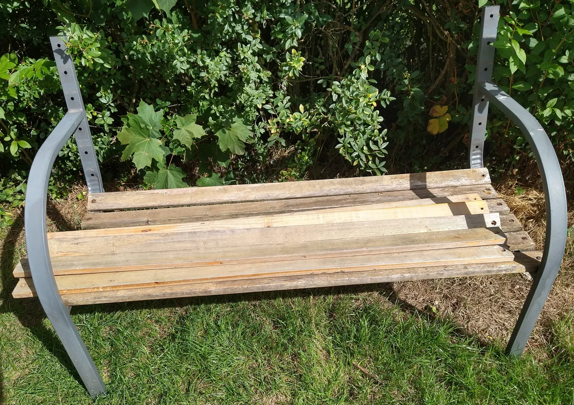 Eine unfertige Gartenbank mit einem Metallgestell und Holzlatten.