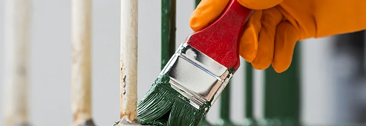 Hand mit Pinsel streicht Metallzaun