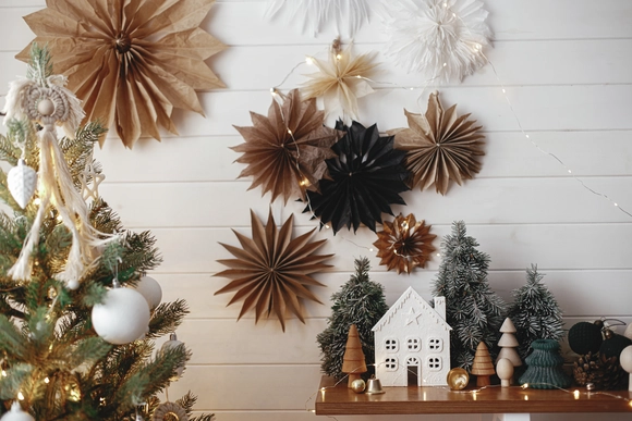 Moderne Weihnachtsdeko mit Papiersternen, Tannenbaum und Miniaturhaus.