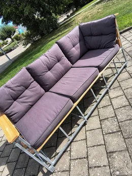 Ein langes Gartensofa mit grauen Polstern auf einem Gestell aus Metall und Holz.