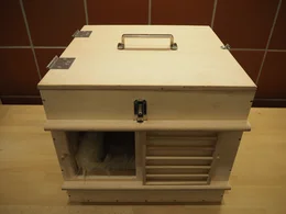 Eine Transportbox aus Holz mit einem flauschigen Tier darin.