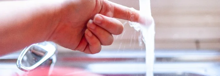 Hand hält Finger unter fließendes Wasser