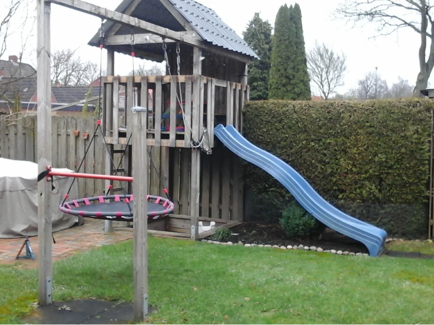 Ein Holzturm mit Rutsche und Nestschaukel im Garten.
