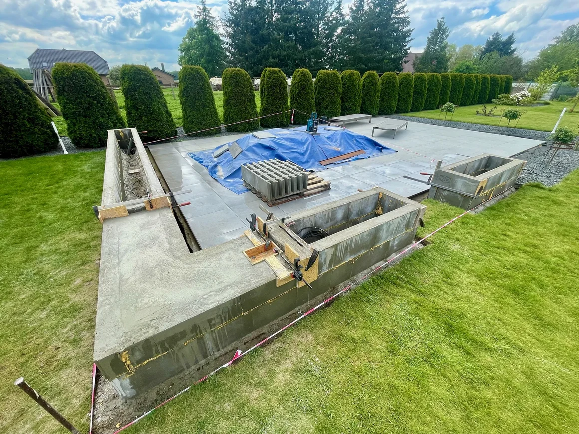 Eine im Bau befindliche Terrasse mit einer L-förmigen Betonmauer im Garten.