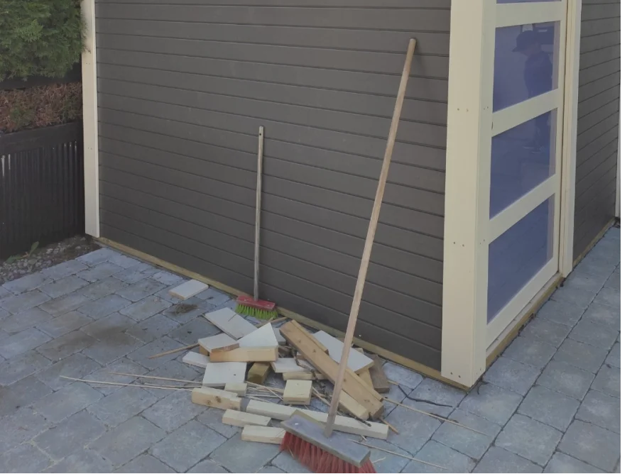 Holzbalken und Besen vor Gartenhaus