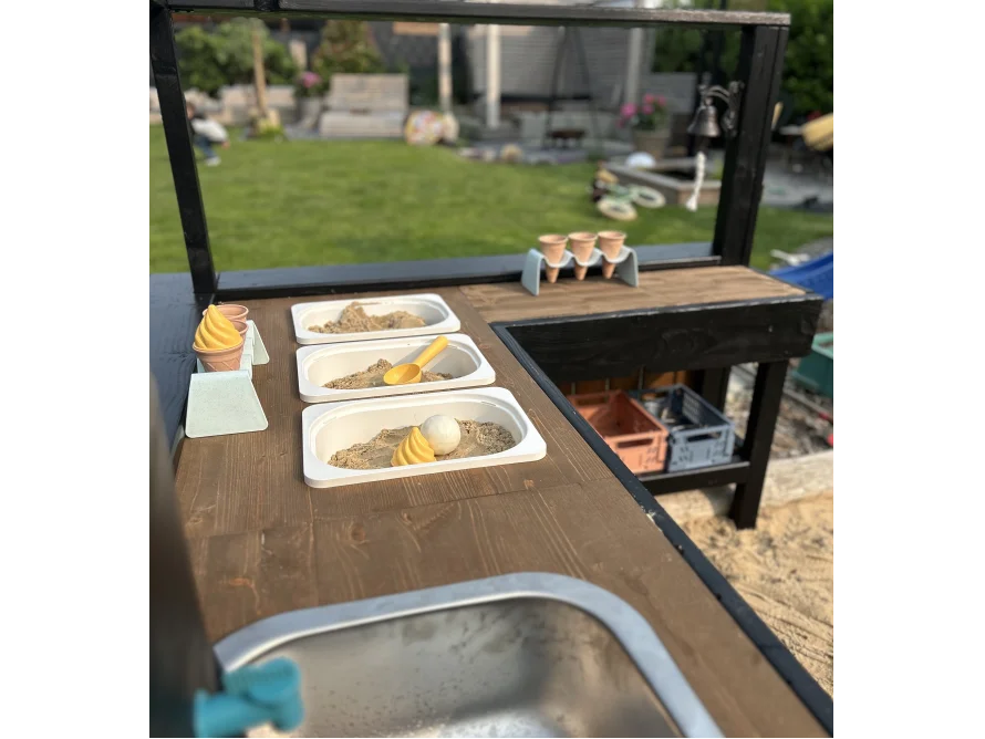 Eine hölzerne Matschküche für Kinder mit Sand und Eisförmchen im Garten.