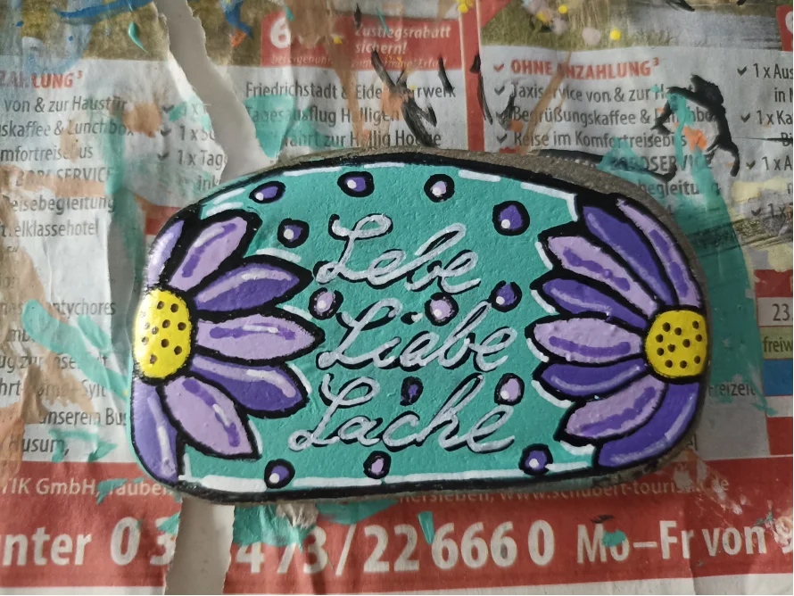 Bemalter Stein mit Blumen und dem Schriftzug Lebe Liebe Lache
