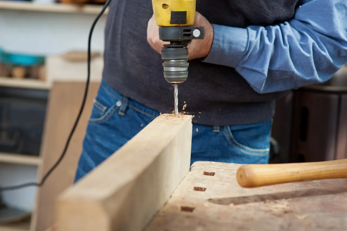 Person bohrt mit einer Bohrmaschine in einen Holzbalken.