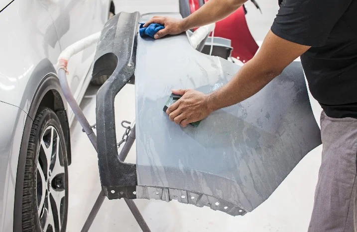 Person schleift Autostoßstange mit Schleifpapier