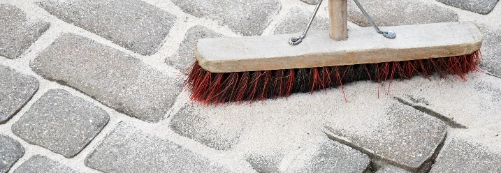 Besen verteilt Sand auf Pflastersteinen