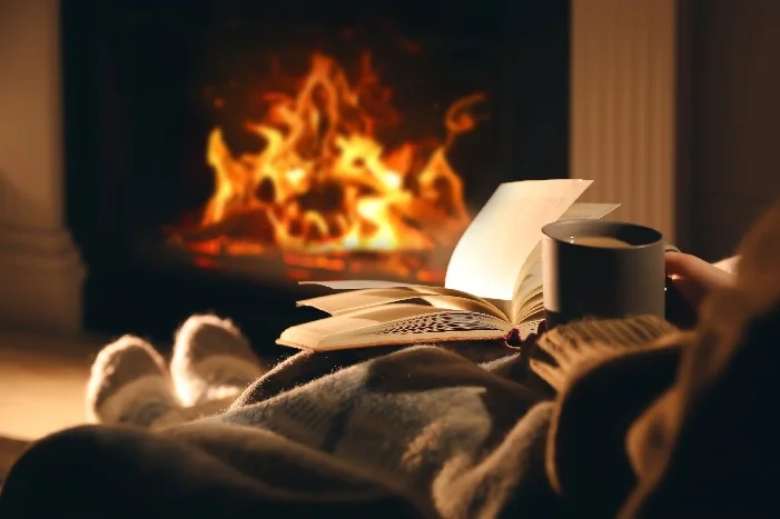 Person mit Tasse und Buch am Kamin
