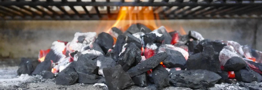 Nahaufnahme von glühender Holzkohle mit Flammen unter einem Grillrost.