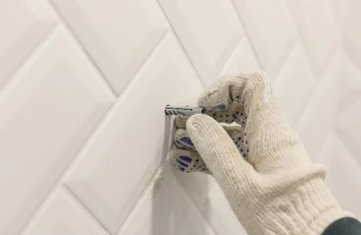 Hand in einem Arbeitshandschuh setzt einen Dübel in eine weiße Wand