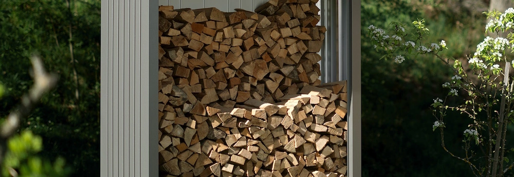 Ein Biohort-Brennholzlager voller Holzscheite steht in einem Garten