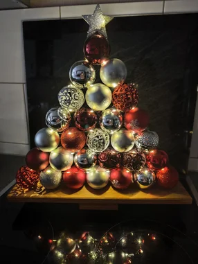 Ein Weihnachtsbaum aus Christbaumkugeln mit Lichterkette und Stern an der Spitze.
