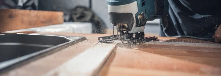 Person sägt Holzplatte mit Stichsäge
