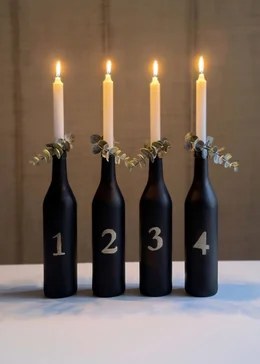 Vier schwarze, nummerierte Flaschen mit brennenden Kerzen als moderner Adventskranz.