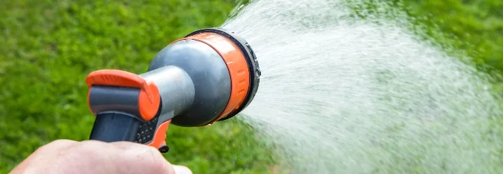 Hand hält Gartenschlauch und bewässert Rasen
