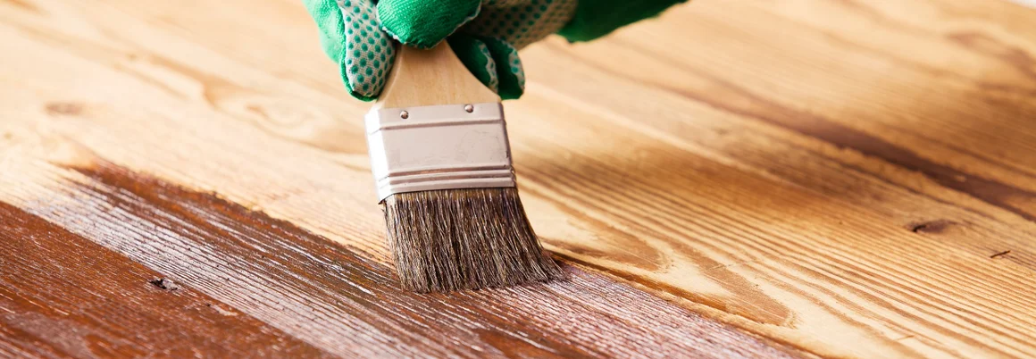 Hand mit Pinsel streicht Holz braun
