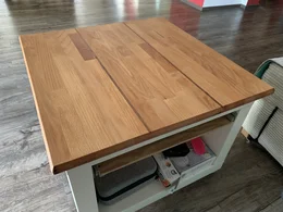 Ein quadratischer Couchtisch mit einer Tischplatte aus Holz und einem weißen Untergestell.