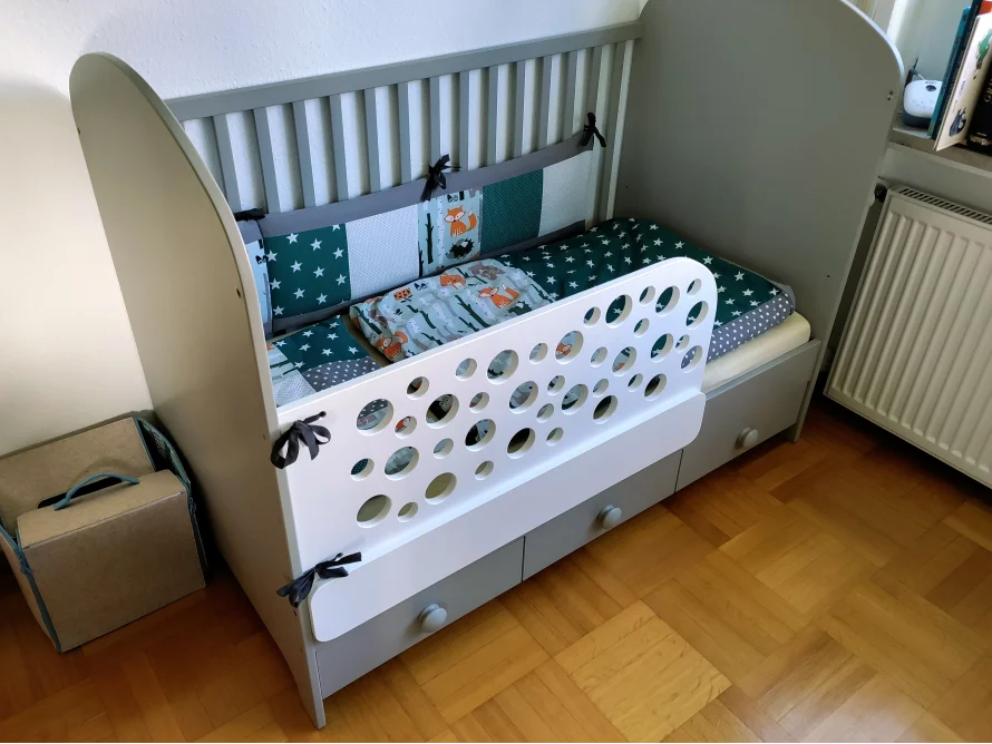 Graues Kinderbett mit Rautenmuster und Nestchen