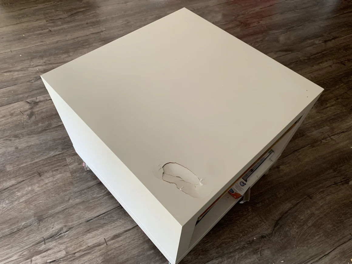 Ein weißer, würfelförmiger Tisch mit einer beschädigten Oberfläche auf einem Holzboden.