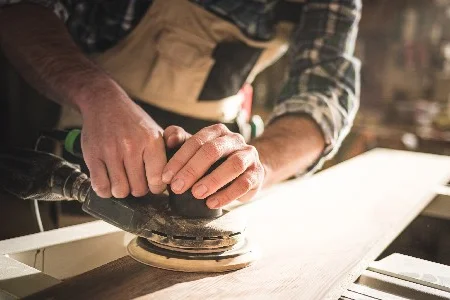 Person schleift Holz mit Schleifmaschine