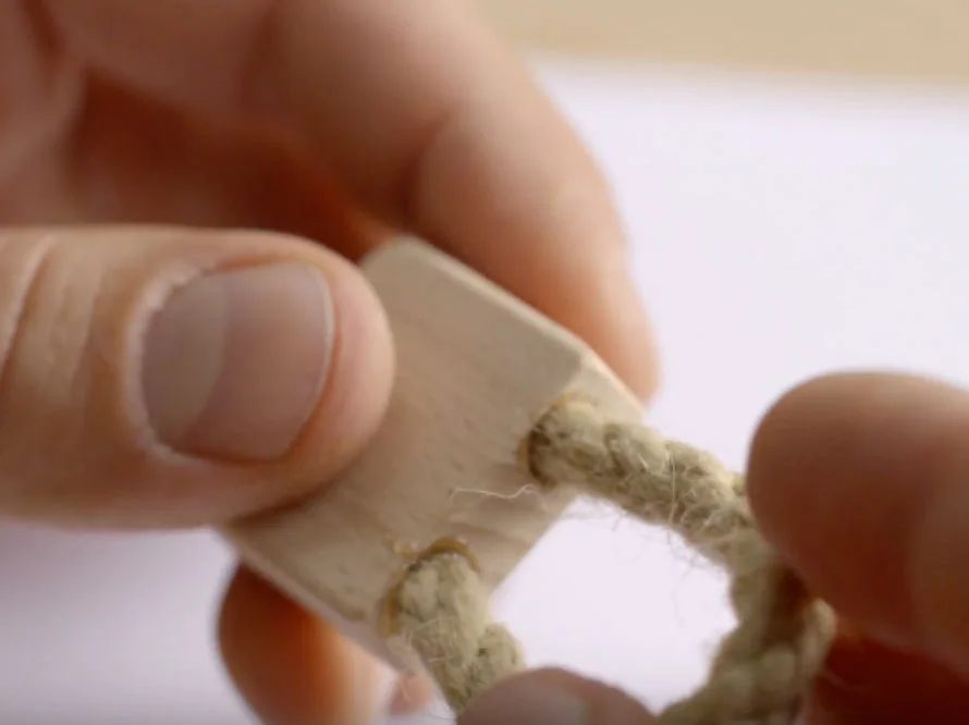 Finger fädeln ein Seil durch einen Holzblock.