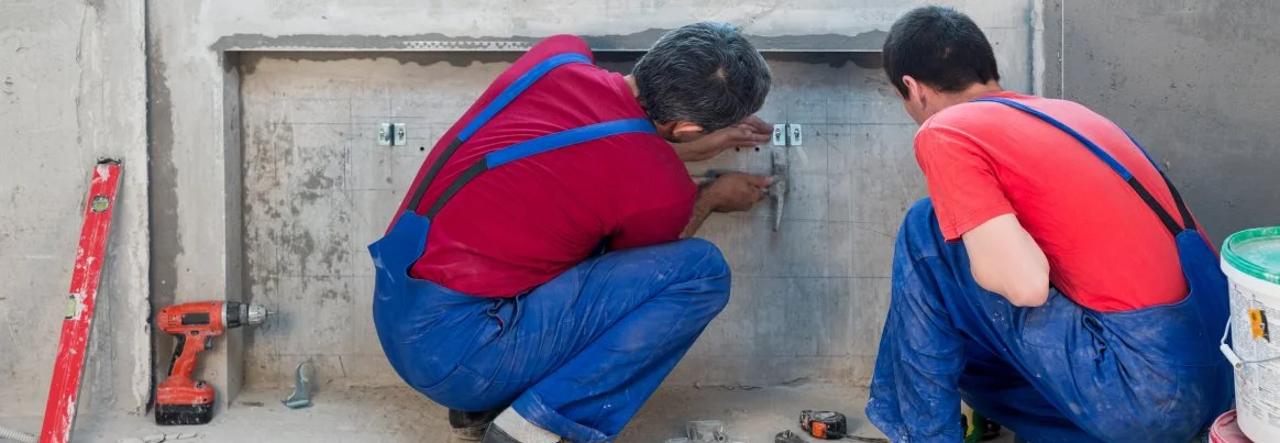 Zwei Handwerker mauern eine Heizungsnische zu.
