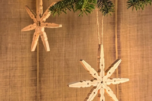 Zwei Weihnachtssterne aus Wäscheklammern an einem Tannenzweig.