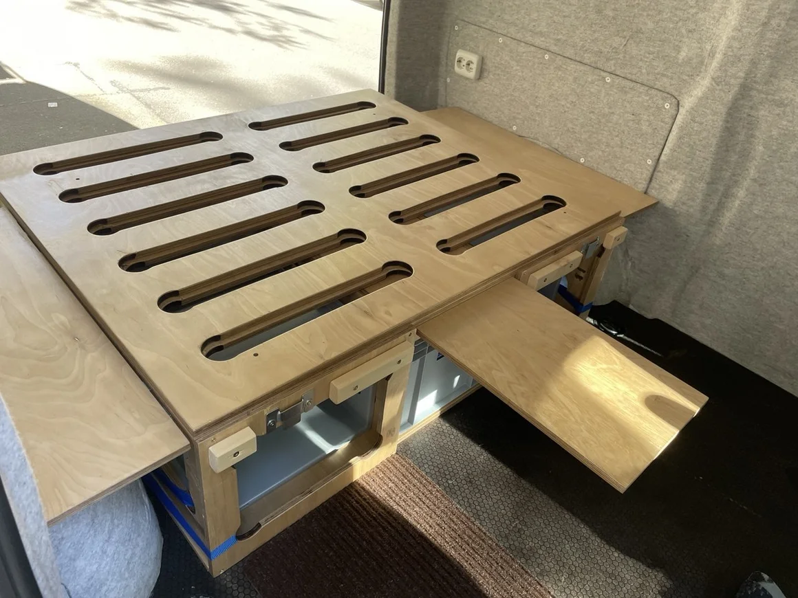 Ausziehbares Holzbett in einem umgebauten Transporter.