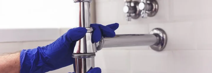 Hände mit blauen Handschuhen montieren einen Siphon