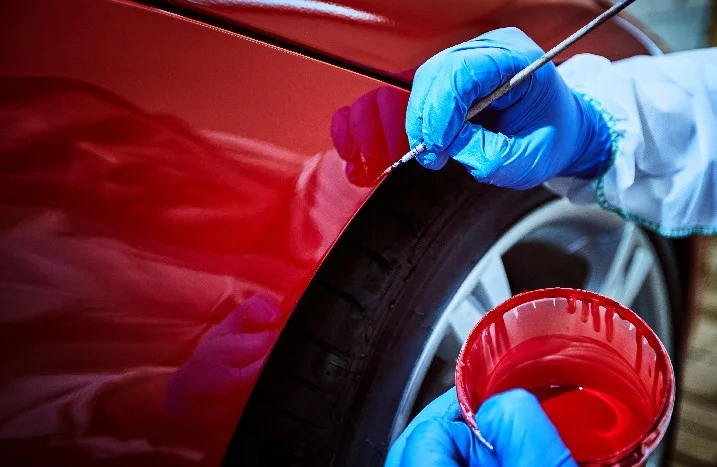 Person lackiert ein rotes Auto mit Pinsel