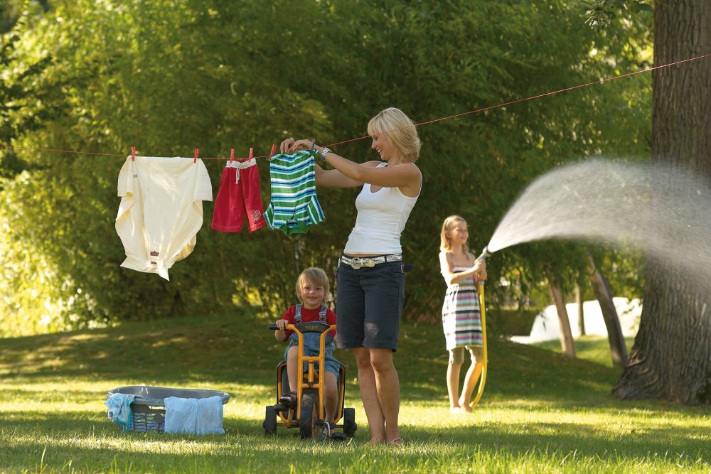 Eine Person hängt Wäsche auf im Garten und Kinder spielen im Hintergrund
