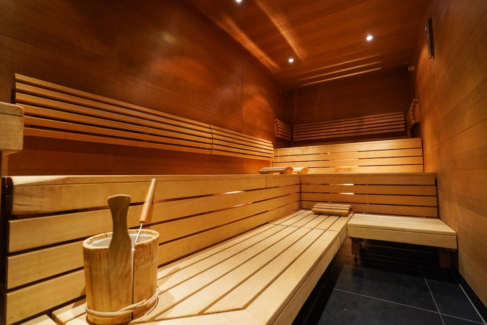 Innenansicht einer leeren, modernen Holzsauna mit Bänken und Aufgusseimer.